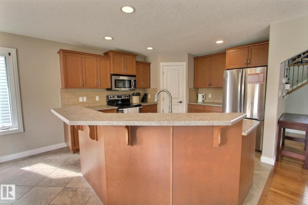 Kitchen with light brown cabinets, granite countertop island with a sink, and stainless steel appliances. - 10 Birchmont Cr, Leduc