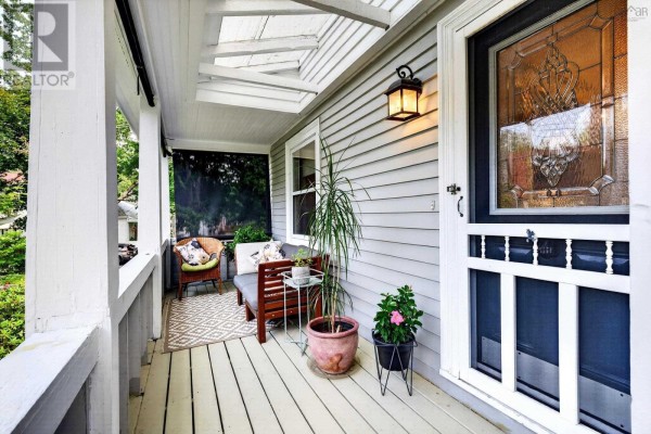 Covered front porch with gray siding, white railings, and a screen door with decorative glass. - 10 Braeburn Road, Halifax