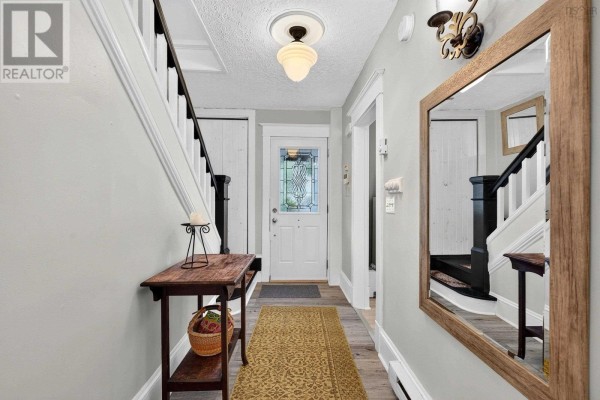 Interior hallway with light grey walls, dark wood staircase, front door, and a large wooden mirror. - 10 Braeburn Road, Halifax