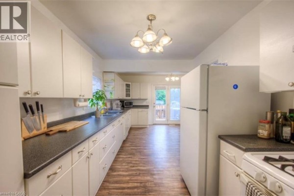 Long kitchen with white cabinets, dark countertops, and stainless steel appliances, view of backyard. - 10 Bruce Street, Brantford