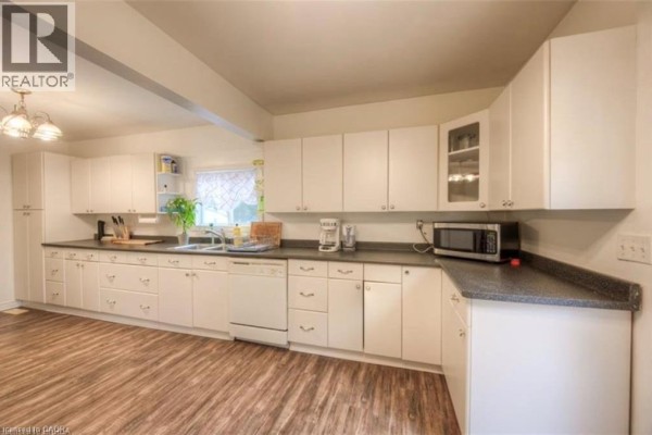 Kitchen with white cabinets, dark countertops, dishwasher, microwave, and sink. - 10 Bruce Street, Brantford