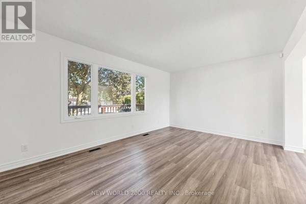 Living room with white walls, large window overlooking deck, and wood-look laminate flooring. - 10 Buce Avenue, Bradford West Gwillimbury