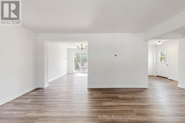 Spacious living area with white walls, neutral flooring, and doorways to dining area and front entrance. - 10 Buce Avenue, Bradford West Gwillimbury