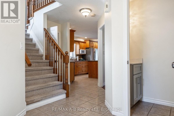 Interior foyer with a staircase, tiled floor, and view into a wooden kitchen. - 10 Buckingham Drive, Stratford