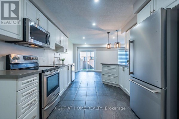 Open concept living area with grey tile floors, white kitchen cabinets, and stainless steel appliances. - 10 Cittadella Boulevard, Hamilton