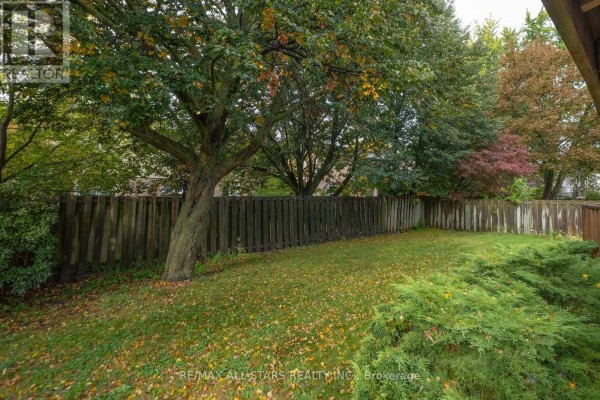 Backyard with green grass, a wooden fence, trees, and scattered autumn leaves. - 10 Colette Drive, Whitby