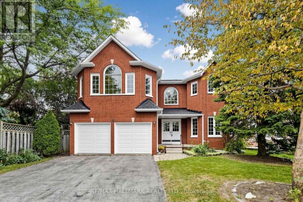 Front exterior of a large red brick house with a white front door, two garage doors, and manicured landscaping. - 10 Driftwood Court, Richmond Hill