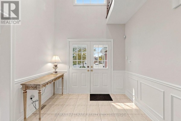 Interior foyer with cream-colored tiled floors, white wainscoting, and double glass doors leading outside. - 10 Driftwood Court, Richmond Hill