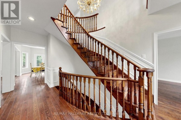 Wide wooden staircase with ornate railings ascends to the upper floor, featuring hardwood floors and a chandelier. - 10 Driftwood Court, Richmond Hill