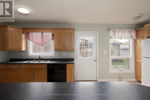 Kitchen with light wood cabinets, black countertops, sink, dishwasher, and a back door. - 10 Dunsford Crescent, St  Marys