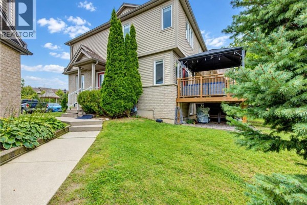 Side exterior view of a beige townhouse with a wooden deck and green trees. - 10 Foxglove Crescent Unit# 40, Kitchener