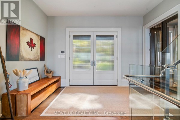 Interior hallway with dark wood floors, a modern floating staircase with glass railings, and artwork. - 10 Hiawatha Avenue, Wasaga Beach