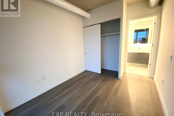 Empty bedroom with white walls, sliding closet doors, and view into bathroom. - 10 James #417 Street, Ottawa