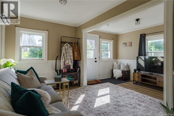 Living room with sofa, television, entryway, and windows looking out to greenery. - 10 Jardine Street, Saint John