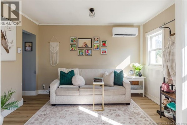 Living room featuring a sofa, macrame wall hanging, framed family photos, and an AC unit. - 10 Jardine Street, Saint John
