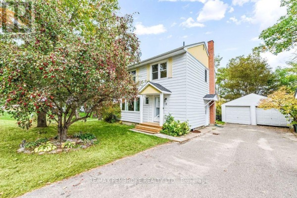 Side exterior view of the white house with yellow accents and a detached garage. - 10 Laurier Avenue, Deep River