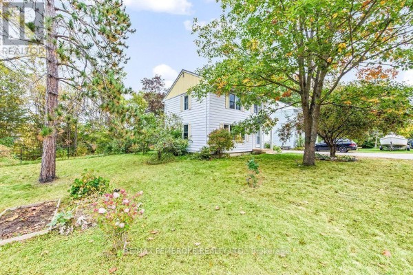 Side view of the house from the lawn, featuring green grass and mature trees. - 10 Laurier Avenue, Deep River