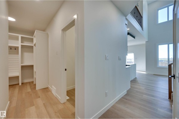 Hallway with light wood floors, white walls, built-in shelving, and an open view to the living area. - 10 Owl Ridge Cl, Fort Saskatchewan