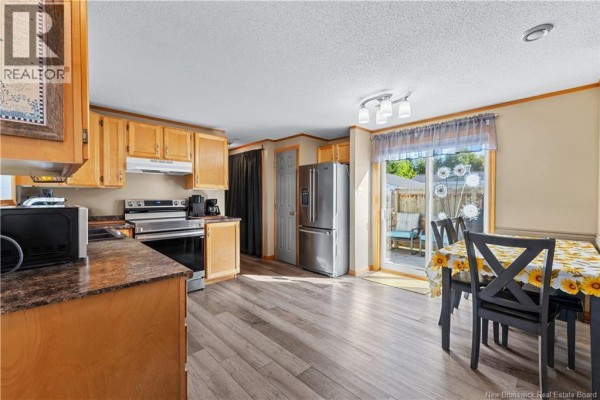 Living room with a sofa, recliners, large window, and an open view to the kitchen. - 10 Peridot Street, Moncton