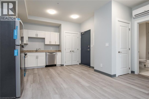 Apartment interior showing kitchen, living area, and doorway to bathroom, with light grey walls and grey flooring. - 10 Queen Street Unit# 203, St  Thomas