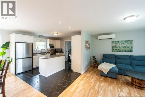 Open concept living area with hardwood floors, a white kitchen island, and stainless steel appliances. - 10 Queensbury Drive, Quispamsis