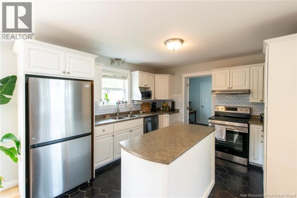 White kitchen cabinets, stainless steel refrigerator, double sink, and dark hexagonal floor tiles. - 10 Queensbury Drive, Quispamsis