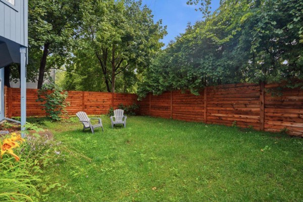 Backyard view with a wooden privacy fence and green grass, two chairs visible. - 10 Rue De Carillon, Gatineau