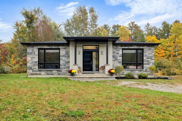 Front view of a single-story house with stone facade, large windows, and a covered entryway with black door. - 10 Rue Lesage, Cantley