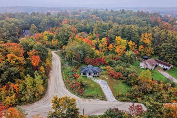 Aerial view of houses surrounded by a dense forest displaying peak fall colors and winding dirt roads. - 10 Rue Lesage, Cantley