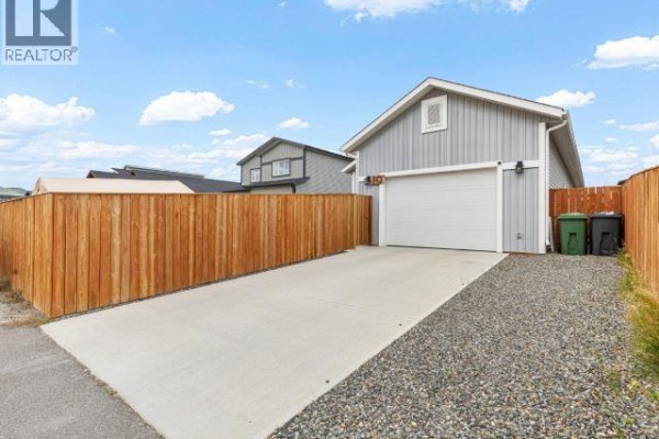Concrete driveway leading to a white garage door on a gray house. - 10 Scotia Lane, Whitehorse