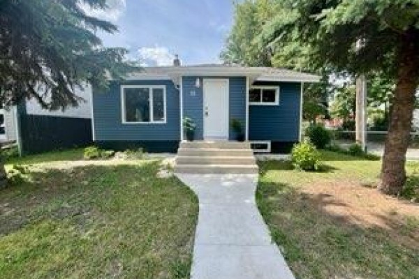 Side view of the house with dark blue siding, white windows, and a chain-link fence. - 10 St Louis Road, Winnipeg