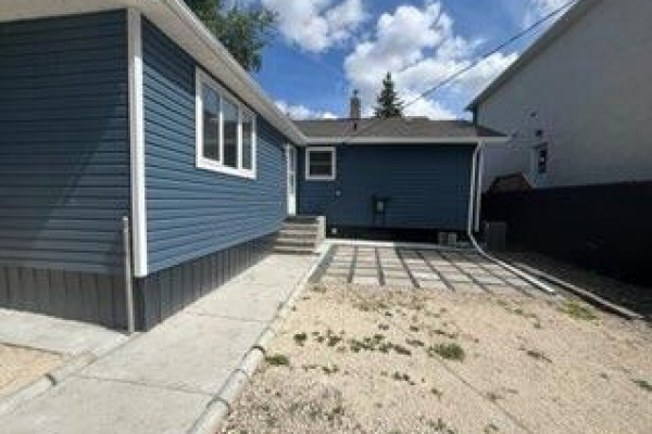 Backyard view of the house and garage with concrete patio and gravel landscaping. - 10 St Louis Road, Winnipeg