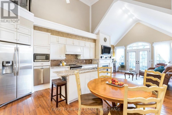 Open-concept kitchen and dining area with white cabinets, stainless steel appliances, granite countertops, and vaulted ceiling. - 10 Wilton Trail, Aurora