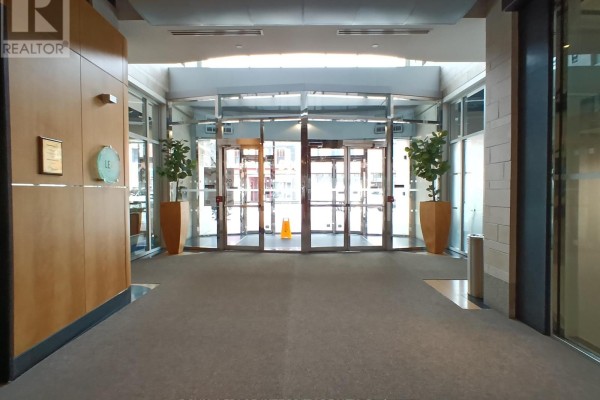 Interior hallway leading to automatic glass doors of a building lobby. Tall potted plants flank the entrance. - 100 - 100 Murray Street, Ottawa