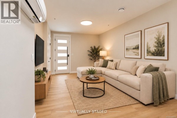 Interior view of a bright living area with light wood floors, leading to a grey-toned kitchen. - 100 2190 Jingle Pot Rd, Nanaimo