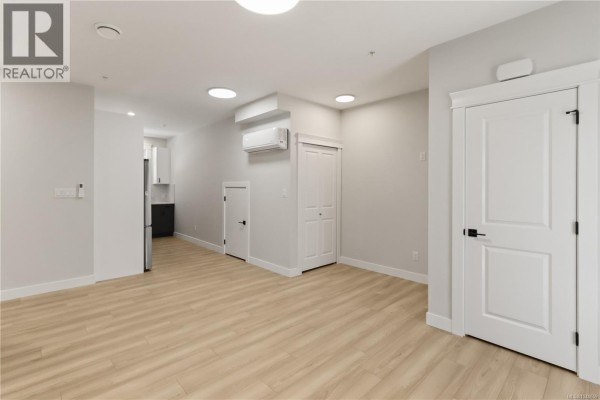 Open concept living space with light wood flooring, white walls, and doors leading to other rooms. - 100 2190 Jingle Pot Rd, Nanaimo