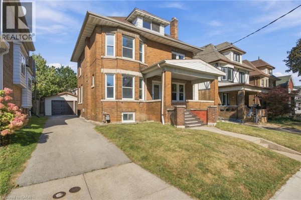 Brick multi-family house with detached garage and driveway on a sunny day. - 100 Balsam Avenue S, Hamilton