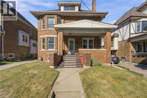 Front exterior of a brick multi-family home with a covered porch and stairs. - 100 Balsam Avenue S, Hamilton