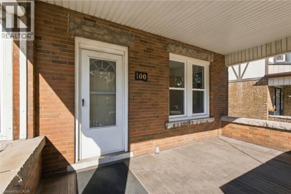 Close-up of the covered porch of a brick house with a white door and windows. - 100 Balsam Avenue S, Hamilton