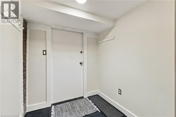 Interior hallway with a white door, white walls, and dark flooring. - 100 Balsam Avenue S, Hamilton