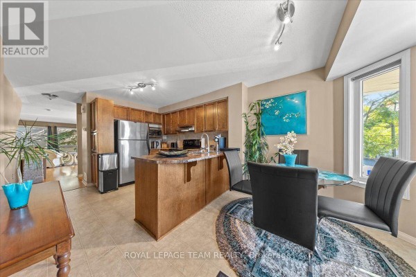 Open concept kitchen and dining area with stainless steel appliances and a glass table. - 100 Bonfield Private, Ottawa