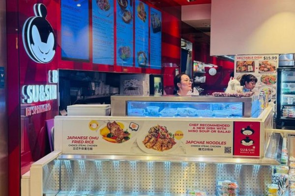 Close-up of a sushi and noodle bar counter showing menu displays and staff behind the counter. - 100 City Centre Drive, Mississauga