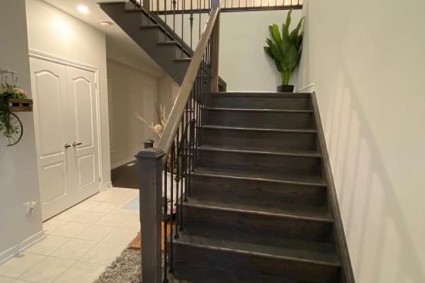 Dark wood staircase with black metal railings leads up from a tiled hallway. - 100 Dolobram Trail, Brampton