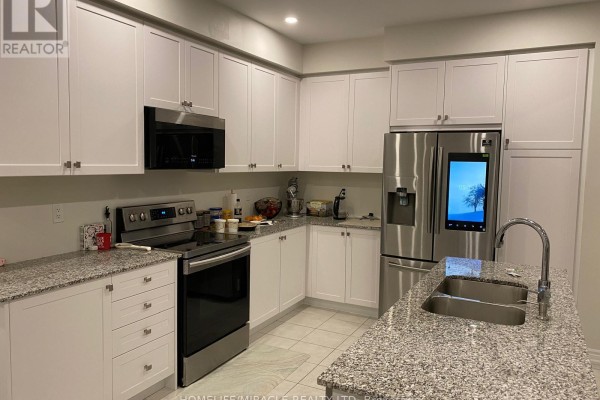 White kitchen with granite countertops, stainless steel appliances, and a double sink island. - 100 Dolobram Trail, Brampton