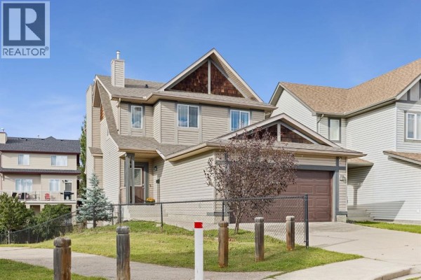 Front exterior of a two-story house with beige siding, a brown garage door, and a chain-link fence. - 100 Evansbrooke Landing Nw, Calgary