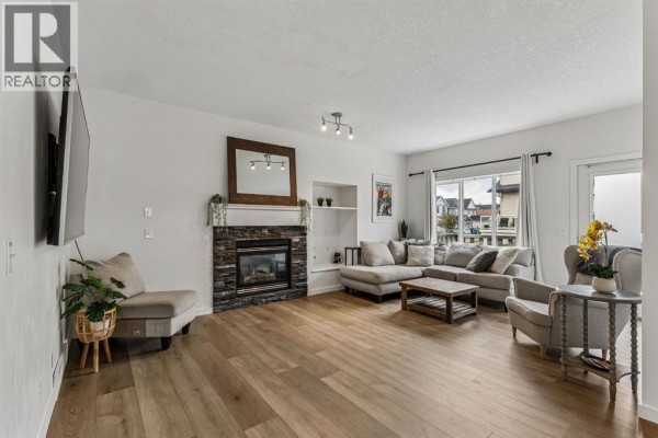 Living room with a stone fireplace, mounted TV, sectional sofa, and light wood flooring. - 100 Evansbrooke Landing Nw, Calgary