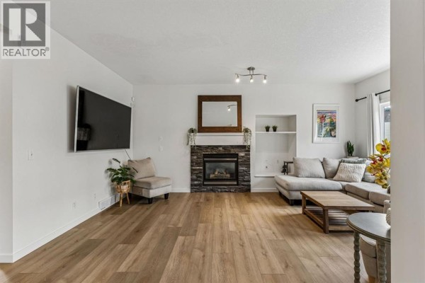 Living room with a stone fireplace, mounted TV, sectional sofa, and light wood flooring. - 100 Evansbrooke Landing Nw, Calgary