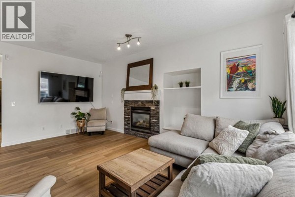 Living room with a stone fireplace, mounted TV, sectional sofa, and light wood flooring. - 100 Evansbrooke Landing Nw, Calgary