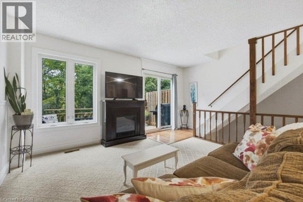 Living room with stairs, beige carpet, sofa, coffee table, and open-concept kitchen. - 100 Inkerman Street Unit# 2, Rockwood