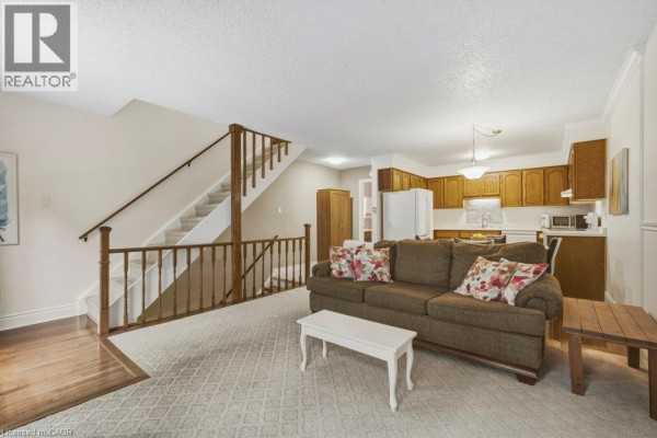 Living room with beige carpet, sofa, coffee table, and kitchen with wood cabinets. - 100 Inkerman Street Unit# 2, Rockwood